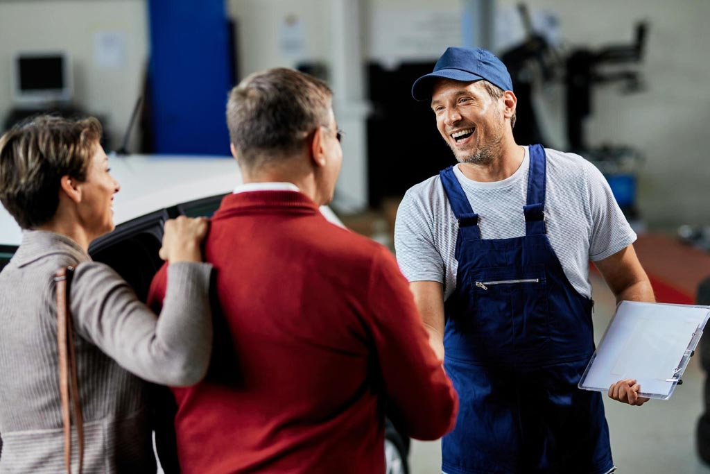 Mecánico saludando a clientes satisfechos, destacando la confianza y el servicio cercano de Shell Lubricants